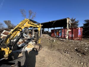 An excavator next to a demolished structure and a red roll-off dumpster from AT Disposal in Dewitt, IA.