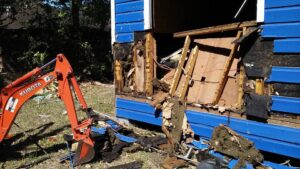 An excavator performing demolition work on a blue building for All Aboard Contractors in Houston, TX.
