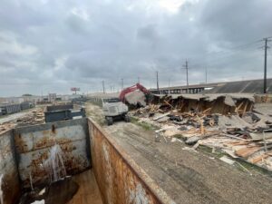 An excavator from White Star Services LLC demolishing a building with roll-off dumpsters in the foreground in Corpus Christi, TX.