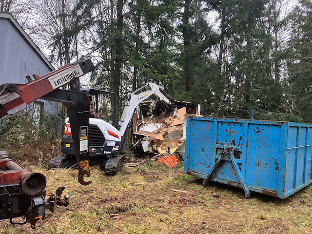 An excavator demolishing a structure with a blue dumpster nearby for debris removal by AAA Rousse Junk Removal Services Inc of Florida in Tampa, FL.