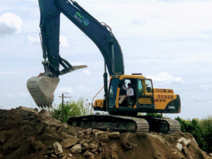 An excavator with the company logo digging into a pile of dirt and debris at Eco Recycling Group in Macon, GA
