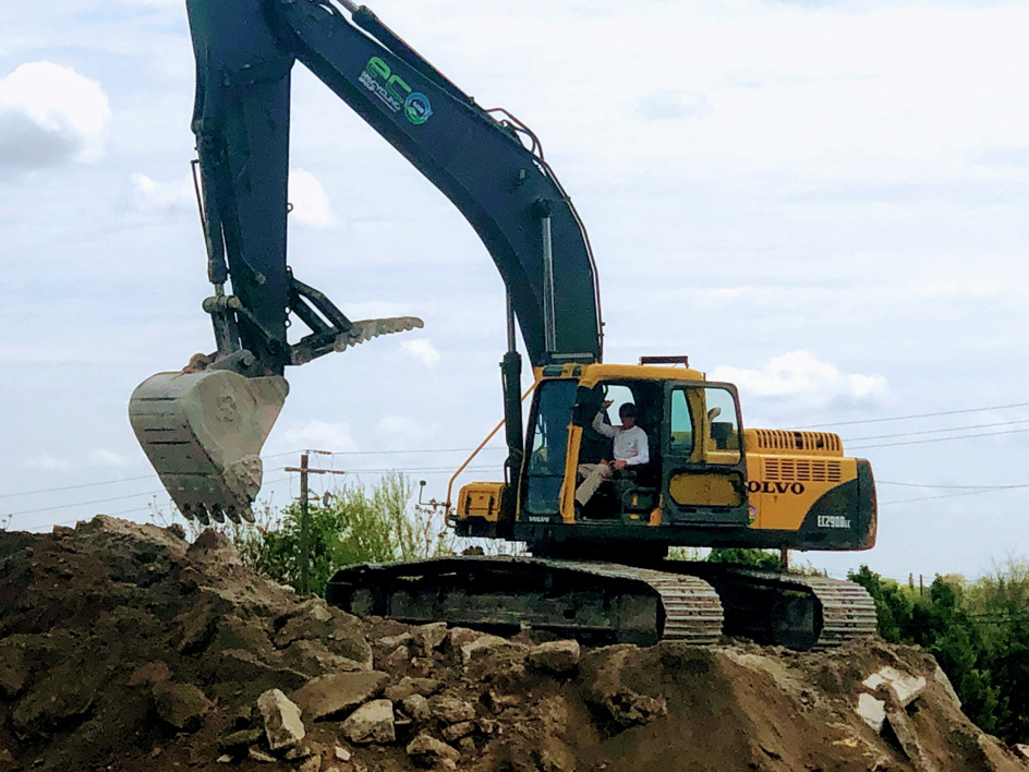 An excavator with the company logo digging into a pile of dirt and debris at Eco Recycling Group in Macon, GA