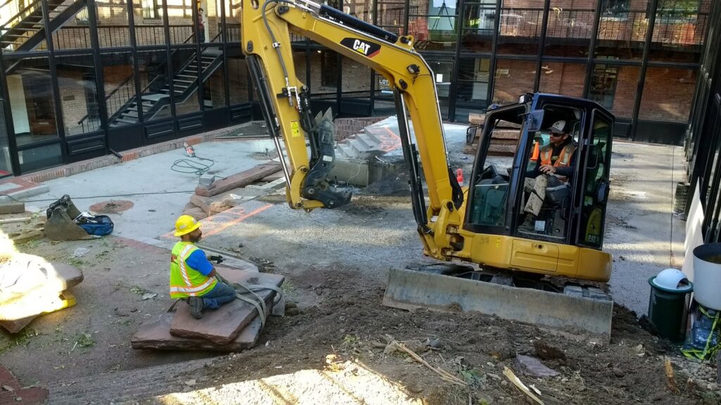 A yellow mini excavator parked next to a large pile of dirt on a residential street by Aspen Excavation in Spokane, WA.