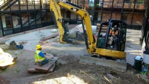 A yellow mini excavator parked next to a large pile of dirt on a residential street by Aspen Excavation in Spokane, WA.