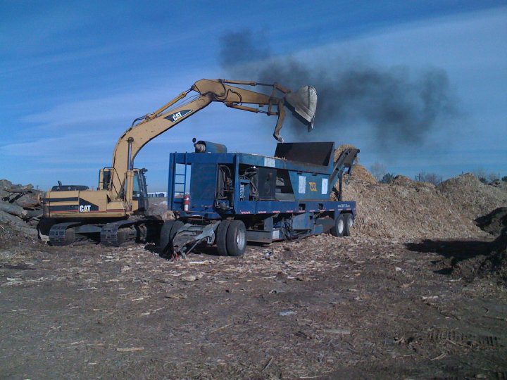 An excavator feeding logs and branches into a large wood chipper for Aesthetic Tree Service in Denver, CO.