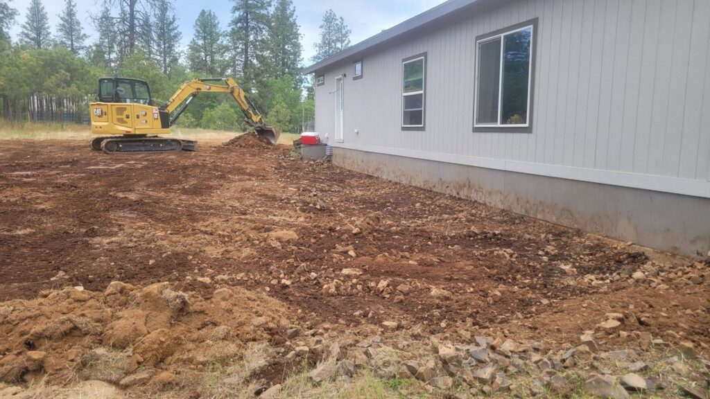 A mini excavator grading the ground around a residential house for Aspen Excavation in Spokane, WA.