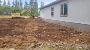 A mini excavator grading the ground around a residential house for Aspen Excavation in Spokane, WA.