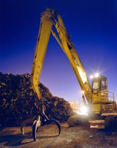 A large yellow excavator with a grapple next to a huge pile of scrap metal at SA Recycling - Long Beach Ave in Los Angeles, CA.