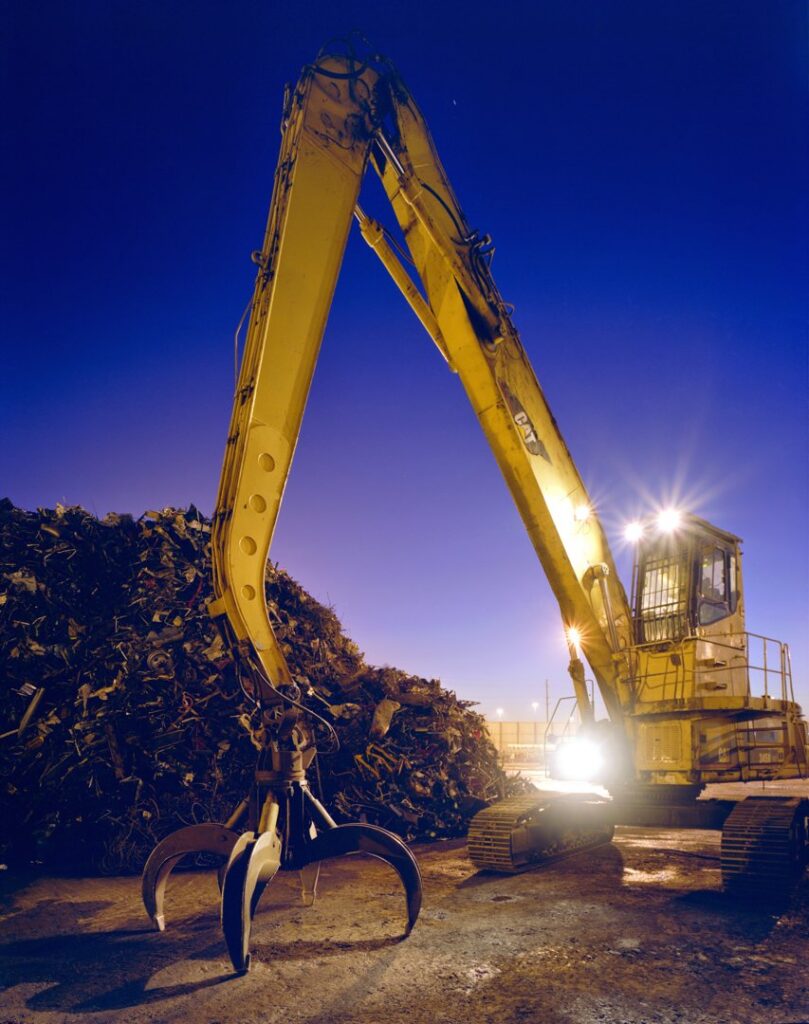 A large yellow excavator with a grapple next to a huge pile of scrap metal at SA Recycling - Long Beach Ave in Los Angeles, CA.