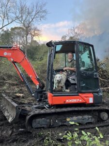 An excavator with an operator and dog performing land clearing for Stewart Tree Service in Mount Pleasant, SC.