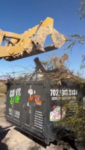 An excavator loading brush and yard debris into a Gone Junkin' Vegas trailer for removal in Henderson, NV.