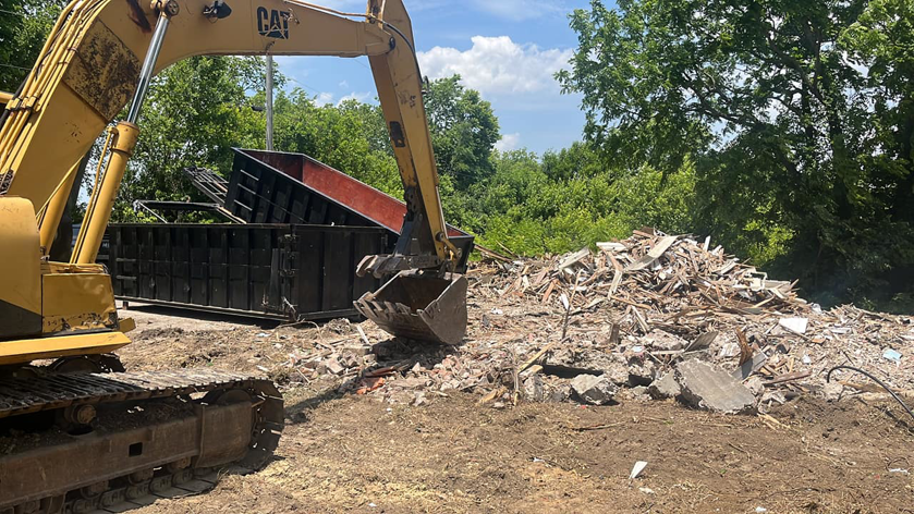 An excavator loading construction debris and rubble into a roll-off dumpster for O'Lakes Dumpster Rental in Lexington, KY.