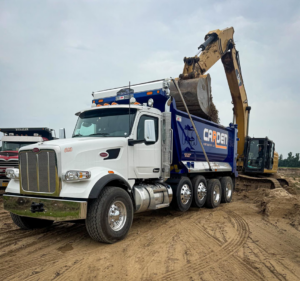 An excavator loading dirt and construction debris into a Carden Contracting LLC dump truck at a job site in Memphis, TN.