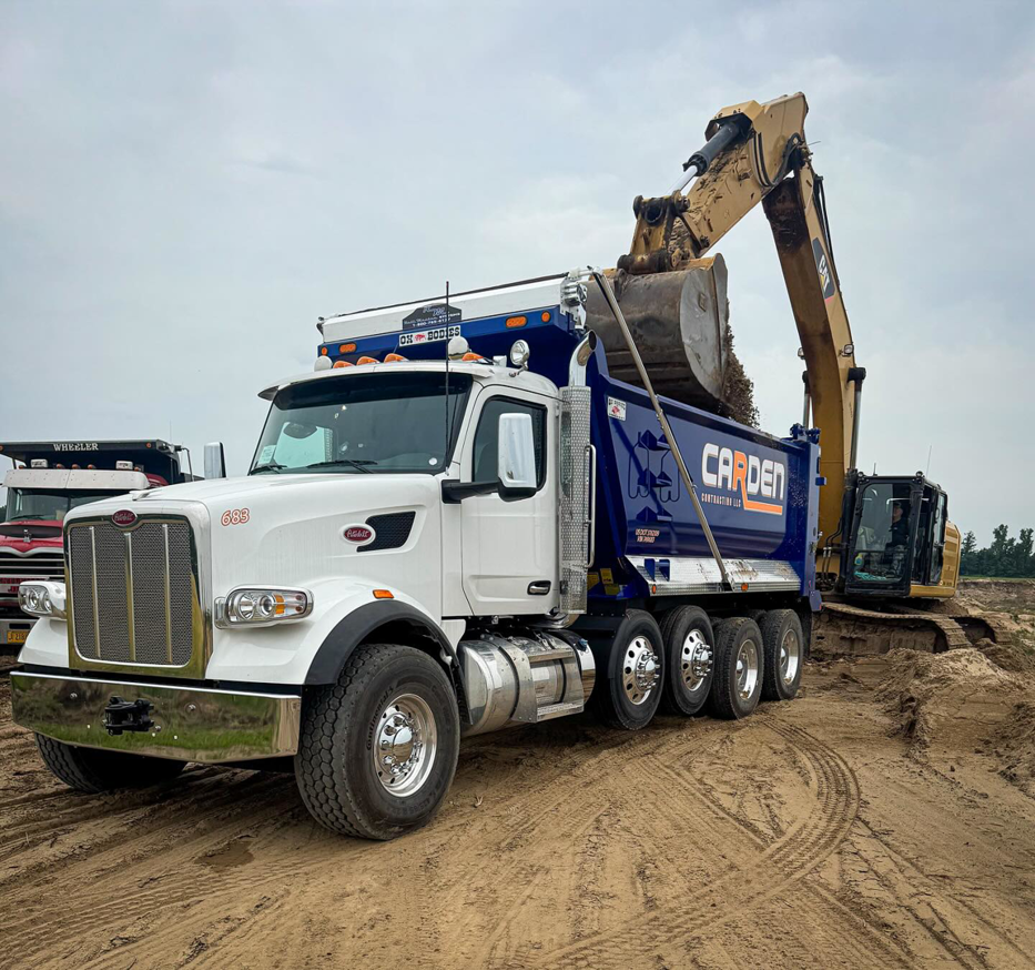 An excavator loading dirt and construction debris into a Carden Contracting LLC dump truck at a job site in Memphis, TN.