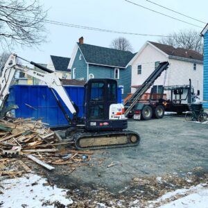 An excavator loading construction debris into an Expert Dumpster roll-off container at a job site in Rochester, NY.