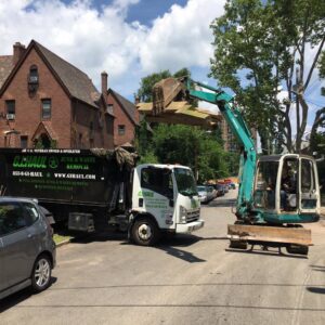 An excavator loading debris into a G.I. HAUL Austin, TX junk removal truck on a residential street.