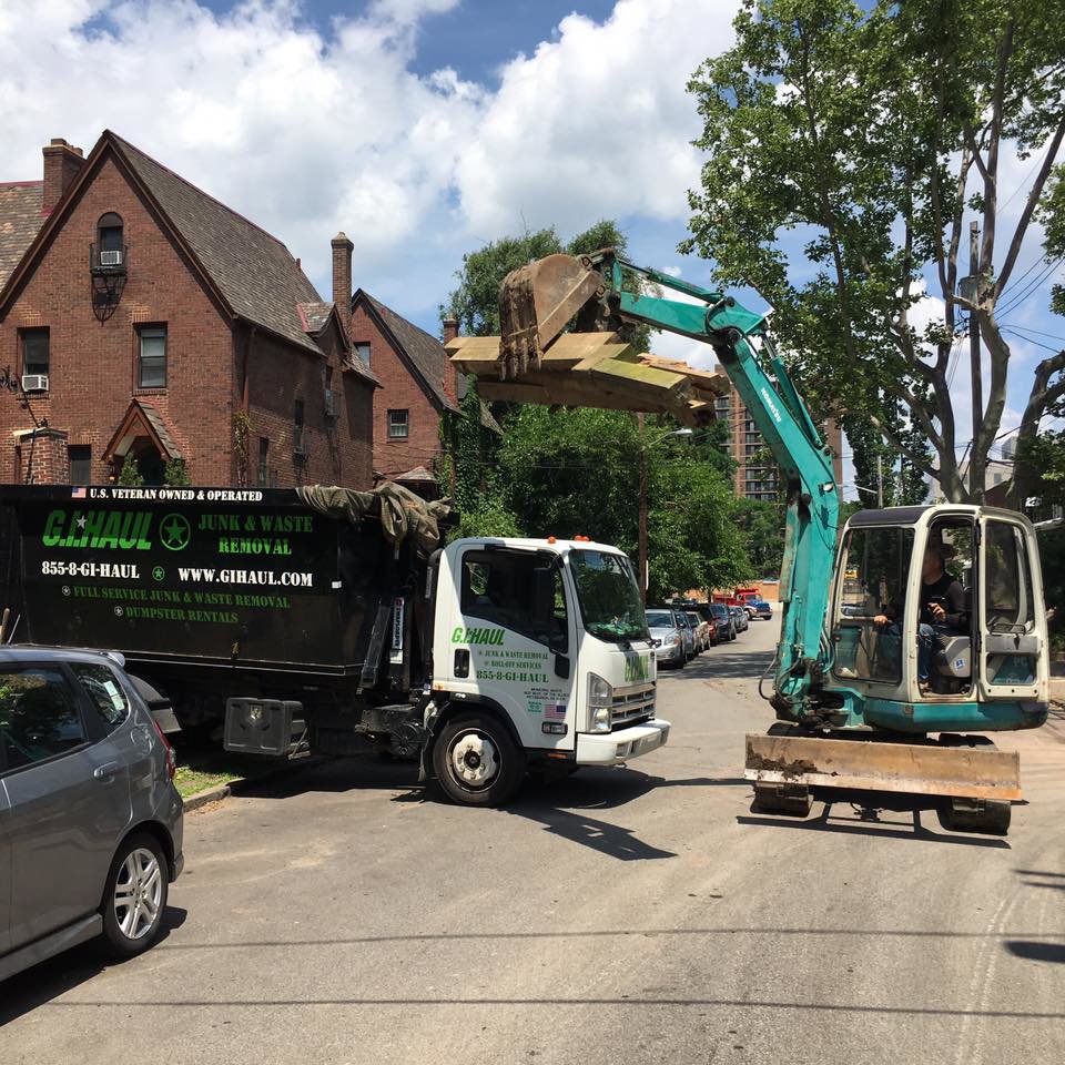 An excavator loading debris into a G.I. HAUL Austin, TX junk removal truck on a residential street.
