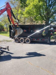 An excavator loading various debris into a black dumpster on an asphalt driveway for Standard Dumpster LLC in Rock Hill, SC.