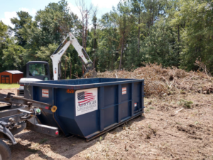 An excavator loads brush and debris into a roll-off dumpster from American Container Services, Inc in Columbia, SC.