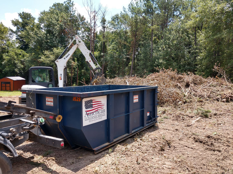 An excavator loads brush and debris into a roll-off dumpster from American Container Services, Inc in Columbia, SC.