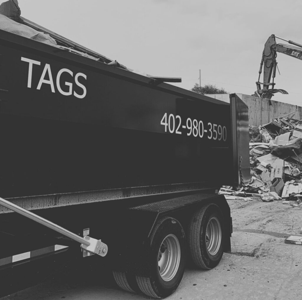 An excavator loading construction debris into a Tags Dumpsters roll-off container at a job site in Omaha, NE.