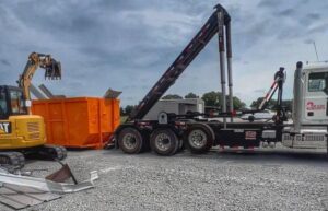 An excavator loading debris into a Tenn-Scrap roll-off dumpster at a job site in Jackson, TN.