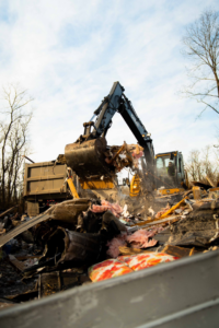 An excavator from Limitless Hauling & Junk Removal loading various junk and debris into a dump truck in Troy, OH.