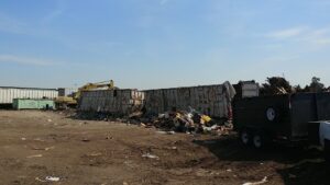 An excavator loading various types of junk and debris into large dumpsters at West Coast Waste in Fresno, CA.