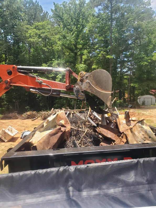 An excavator loading rusty metal debris and construction waste into a dumpster for Standard Dumpster LLC in Rock Hill, SC.