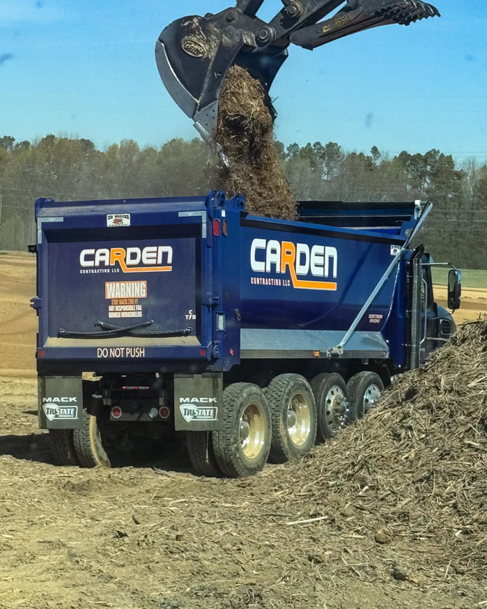 An excavator loading organic waste and brush into a Carden Contracting LLC dump truck for removal in Memphis, TN.