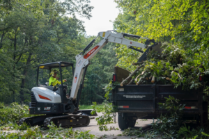 An excavator loading cut tree branches and debris into a trailer for Explore Tree Service in Durham, NC.