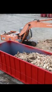 An excavator loading wood debris into a red Geppert Recycling dumpster for efficient junk removal in Philadelphia, PA.