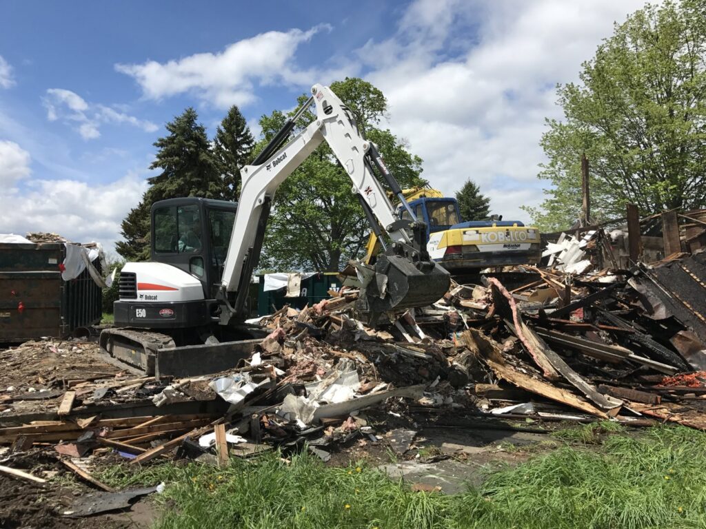 An excavator moving a large pile of demolition debris for junk removal by Expert Dumpster in Rochester, NY.