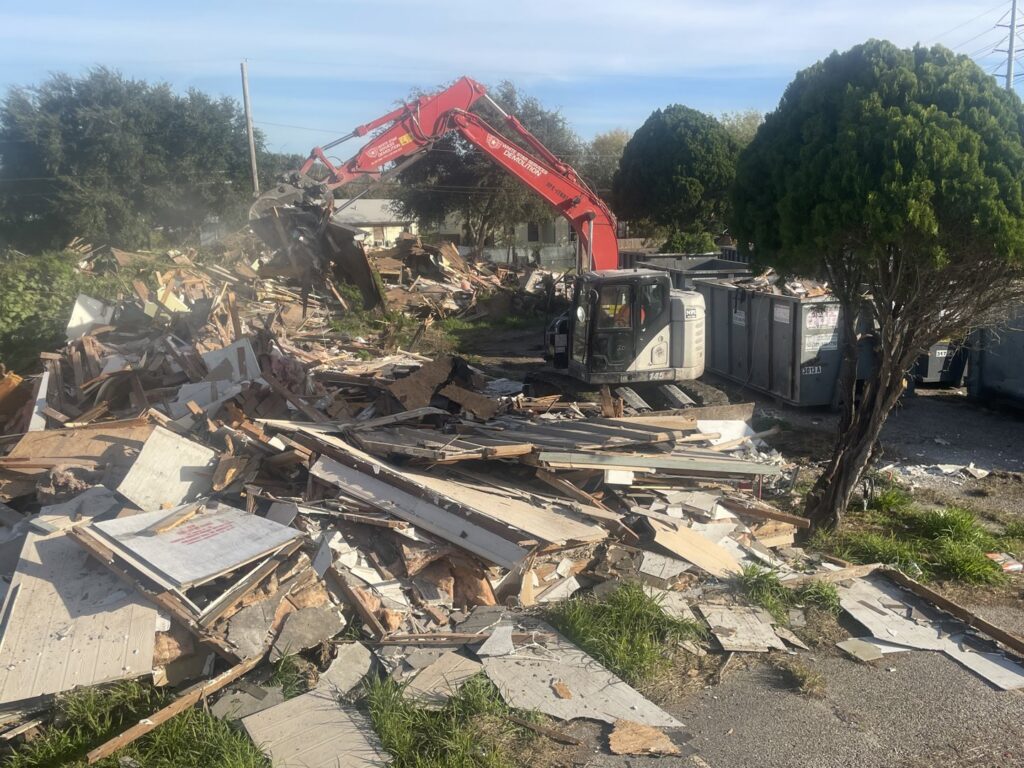 An excavator from White Star Services LLC working on a large pile of mixed demolition debris with dumpsters in the background in Corpus Christi, TX.