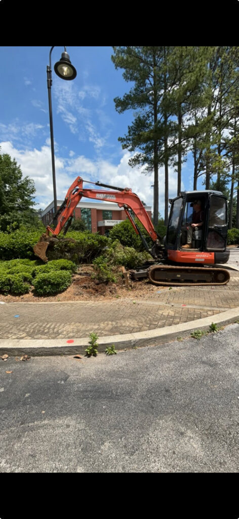 An excavator removing bushes and yard junk as part of a cleanup service by Green Brothers Services in Harvest, AL