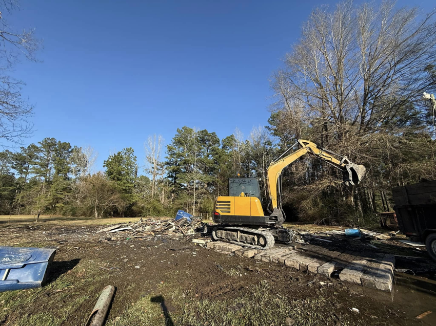An excavator actively removing a large pile of debris and junk for Junk Removal Veterans LLC in Deridder, LA.