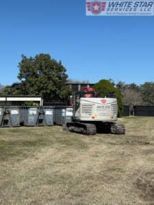 An excavator from White Star Services LLC positioned next to multiple roll-off dumpsters on a job site in Corpus Christi, TX.
