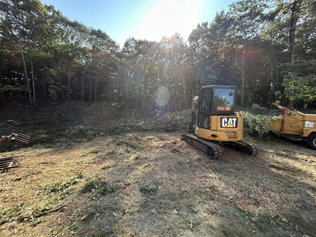 An excavator and wood chipper on a site, showing land clearing services by JTE & Company in Oxford, MA.