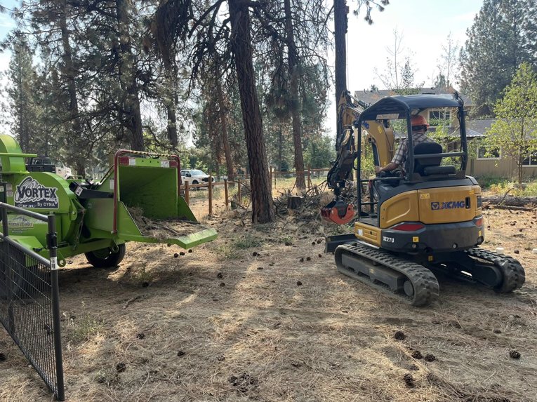 An excavator and a large wood chipper on a job site, processing tree debris for Hiatt Services in Spokane, WA.