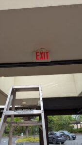 A ladder positioned near an exit sign, indicating repair or installation work by DemoCraft Commercial Services in Everett, WA