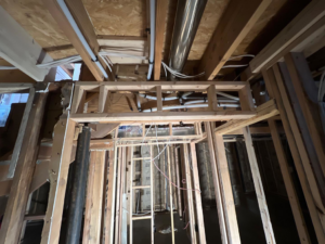 Exposed plumbing pipes and electrical wiring within a framed ceiling and wall structure by Kliesen Construction Company in Pueblo, CO.