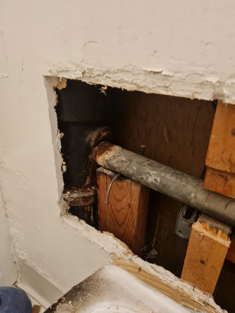 Close-up of exposed, rusty plumbing pipes within an opened wall, indicating repair work by All American Handyman services in Billings, MT