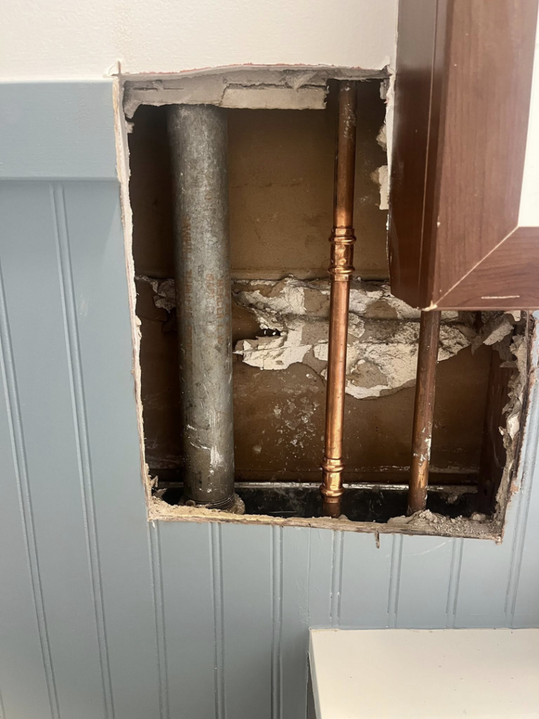 Exposed plumbing pipes in a wall cutout, indicating repair or installation work by Coach Rose Painting Team in Norfolk, VA.