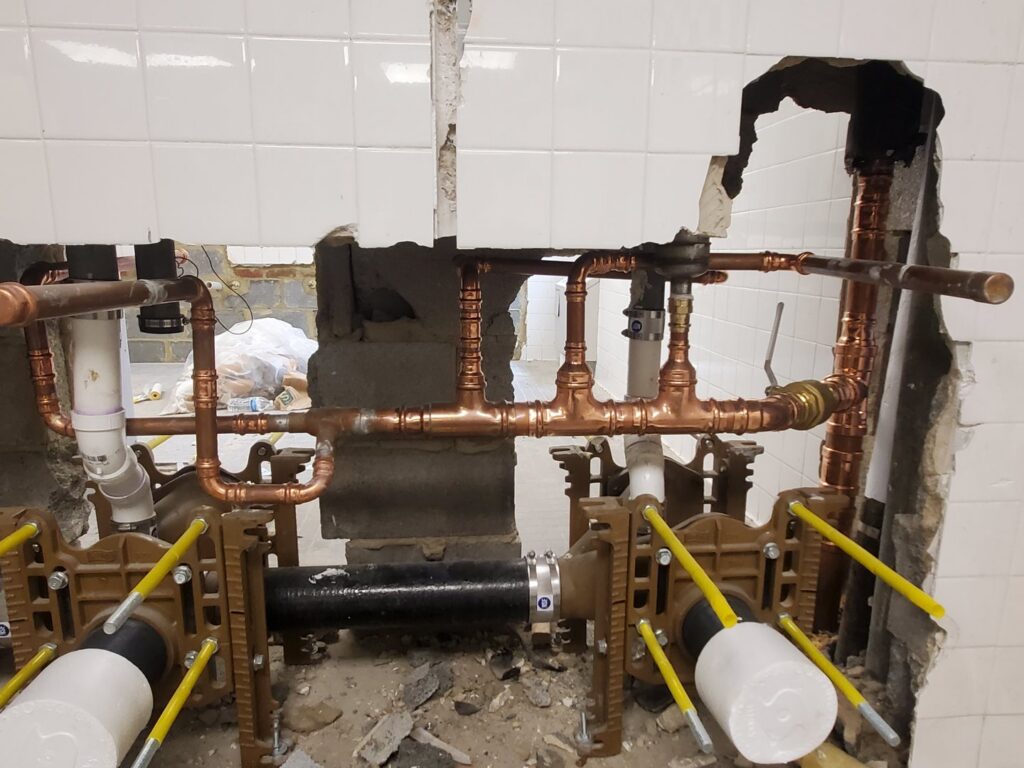 Exposed copper and black plumbing pipes in a wall opening during installation by Snyder Solutions LLC in Richmond, VA