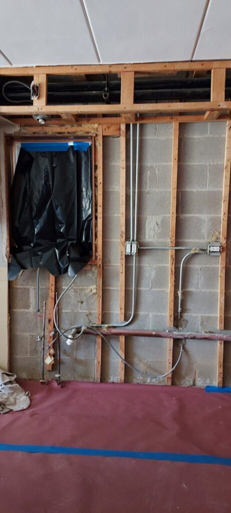 An interior wall with exposed studs, electrical conduit, and plumbing pipes during a renovation by Keeler Construction Group Inc. in Blue Island, IL.