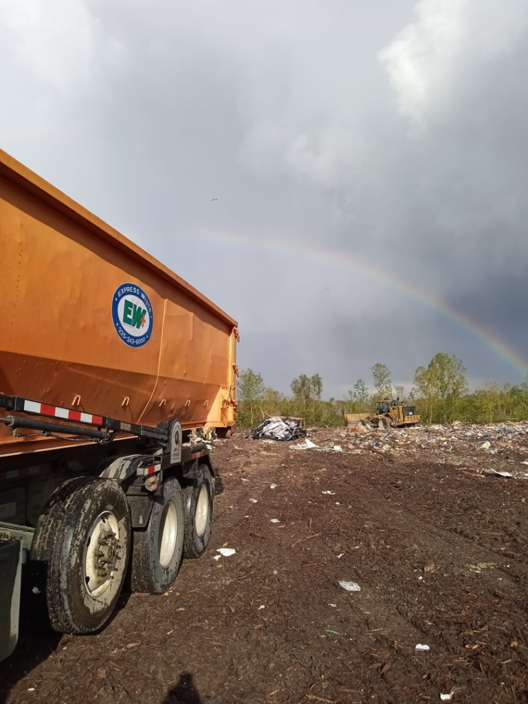 An Express Waste roll-off dumpster at a waste disposal site under a rainbow in Denham Springs, LA.