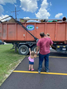 A full Express Waste orange dumpster for junk removal with a family nearby in Denham Springs, LA.