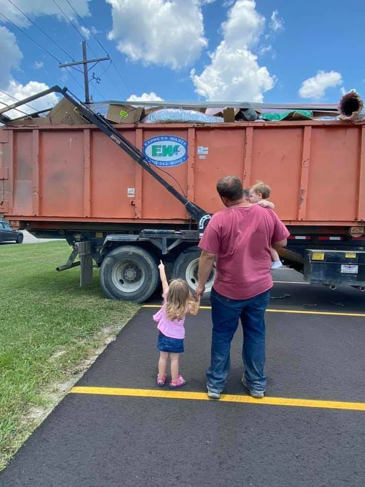 A full Express Waste orange dumpster for junk removal with a family nearby in Denham Springs, LA.