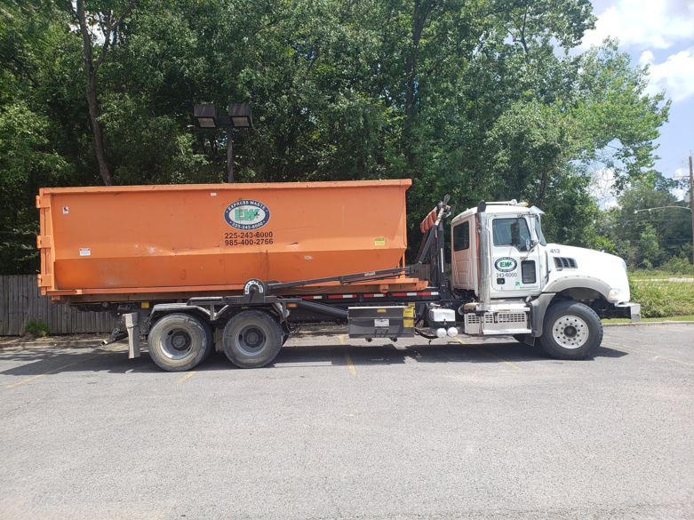 An Express Waste roll-off truck with an orange dumpster parked in Denham Springs, LA.