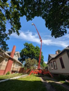 An extended red spider lift positioned between two houses for tree service work by Mountain Tree Company in Missoula, MT.